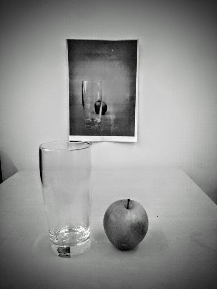 sw Foto von einem leeren Wasserglas und einem Apfel. 
Im Hintergrund an der Wand, ein Foto mit dem gleichen Glas und Apfel.