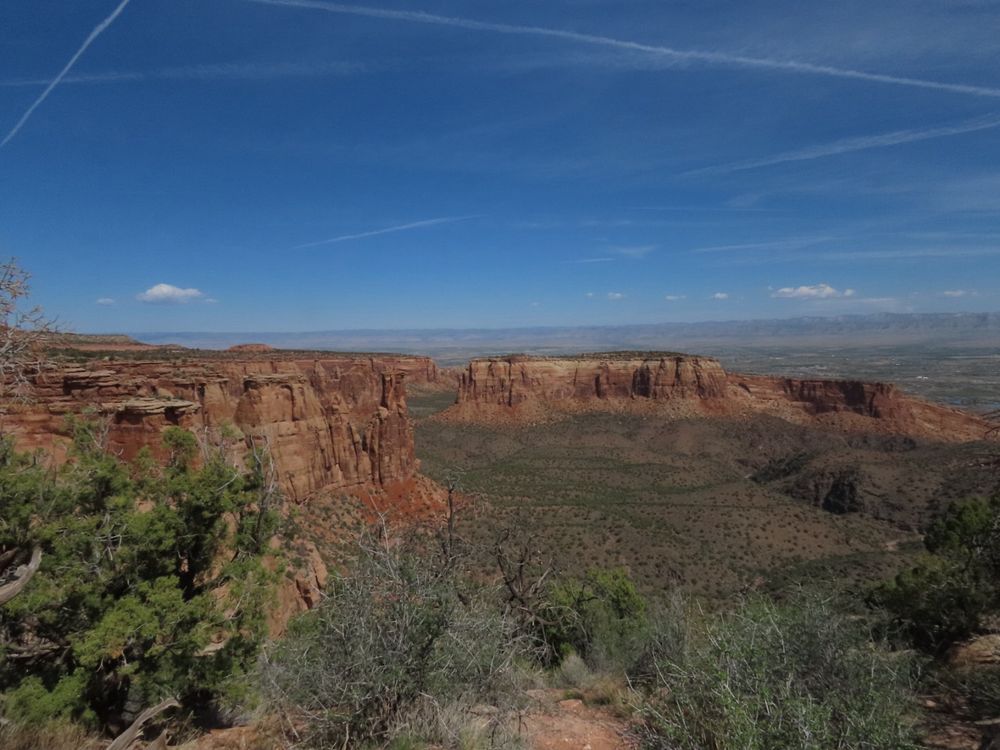 The landscapes of Colorado National Monument. Steep dark orange and red cliffs with a few nice monoliths, above a low plain of pinyon and sage.