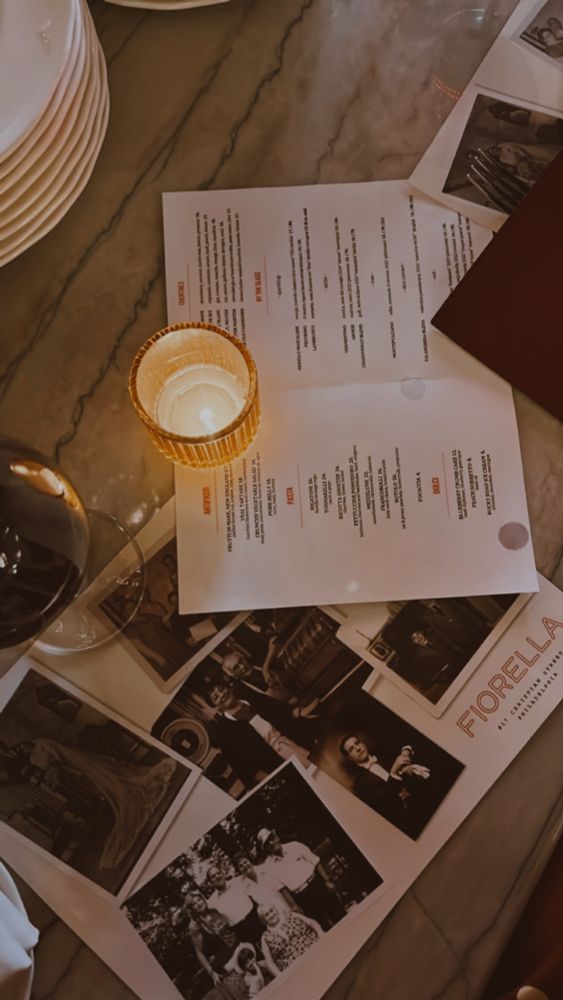 Shot of the brown-marbleish bar top at fantastic Philly restaurant Fiorella. The warm, low-lit shot is from above; several menus are haphazardly laid over one another, there's a single small candle for vibes, and a glass of red wine is off to the left side of the frame. There are white dinner plates stacked off to the top of the frame as the chefs are working behind the bar, right in front of diners. Delicious meal.
