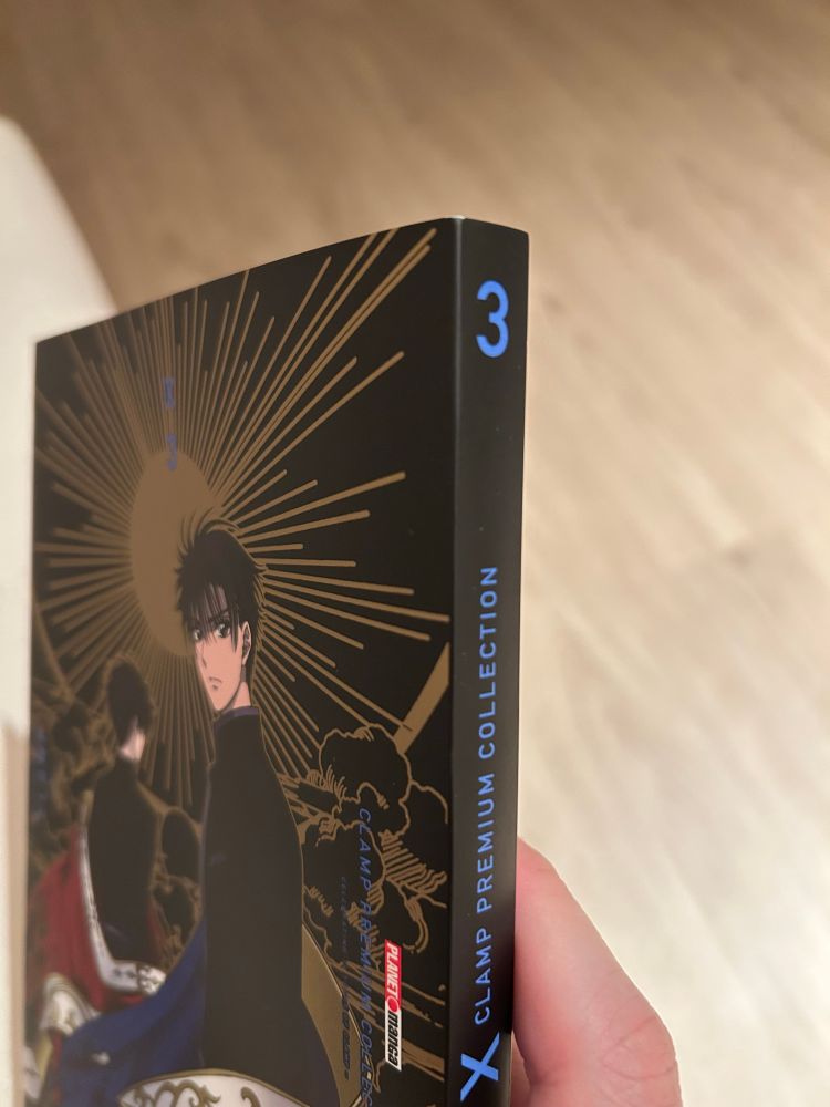 Foto de uma mão direita segurando a edição brasileira do volume 3 de X da edição CLAMP PREMIUM COLLECTION, destacando a lombada.