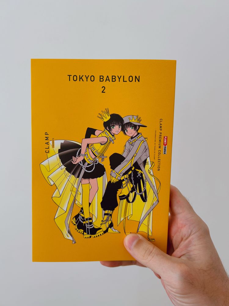 Foto de uma mão direita segurando a edição brasileira do volume 2 de Tokyo Babylon (CLAMP PREMIUM COLLECTION) contra um fundo branco.