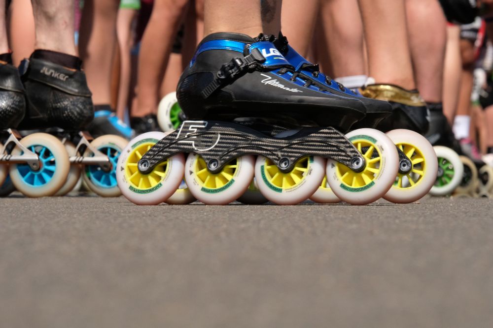 Viele Beine auf Speedskates stehen auf Asphalt.