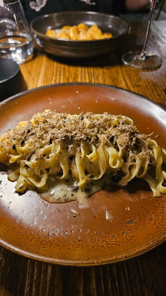 Picture of tagliatelle with black pepper and truffle sauce, served on a brown plate atop a brown oak-like table with a varnish finish.