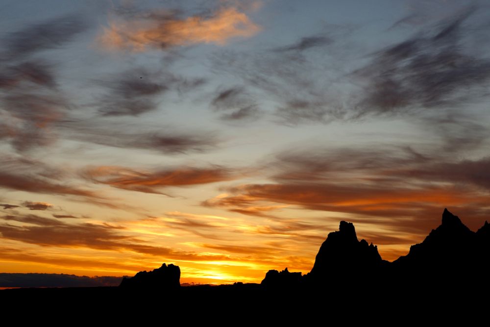 Complex sunset with yellow, orange and black colors and silhouetted rock formations in the foreground.