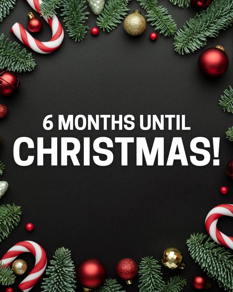 A festive holiday-themed image with a black background bordered by green pine branches, red and gold Christmas ornaments, red and white candy canes, and small decorative berries. In the center, large white text reads: "6 MONTHS UNTIL CHRISTMAS!"