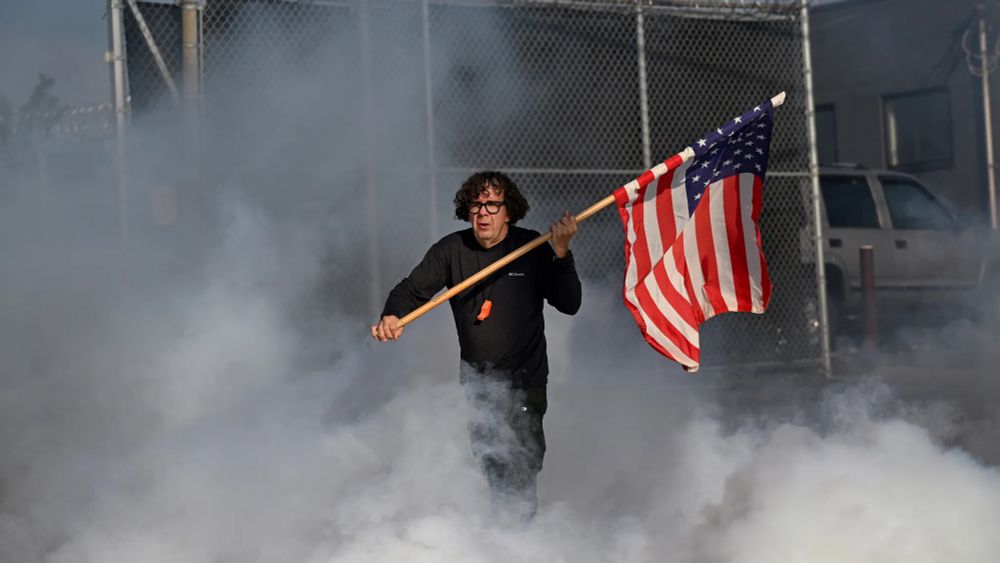 A picture of Curtis Evans walking through tear gas at an ICE facility with an American flag.
