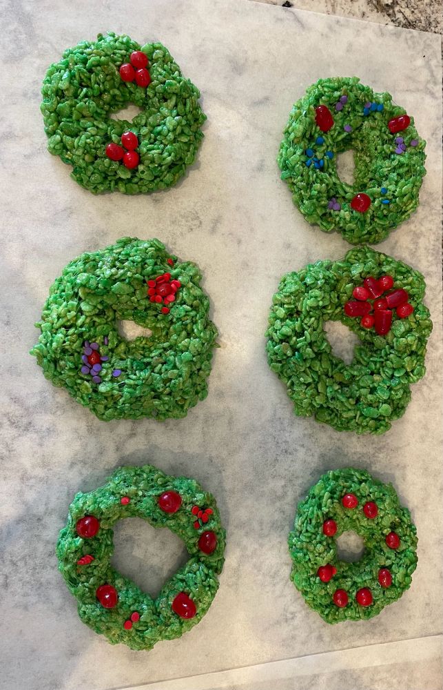 A photo of green rice krispy treats shaped as wreathes, some with red hot tamales and purple sprinkles on top