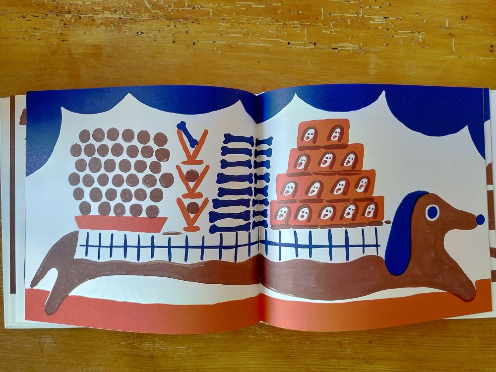 Double page intérieure du livre de Laura Simonati où l'on voit un teckel marron sur toute la largeur avec sur le dos une nappe à carreaux bleue sur laquelle se trouve des plats pour chiens : des os, de la pâtée, des boulettes.
