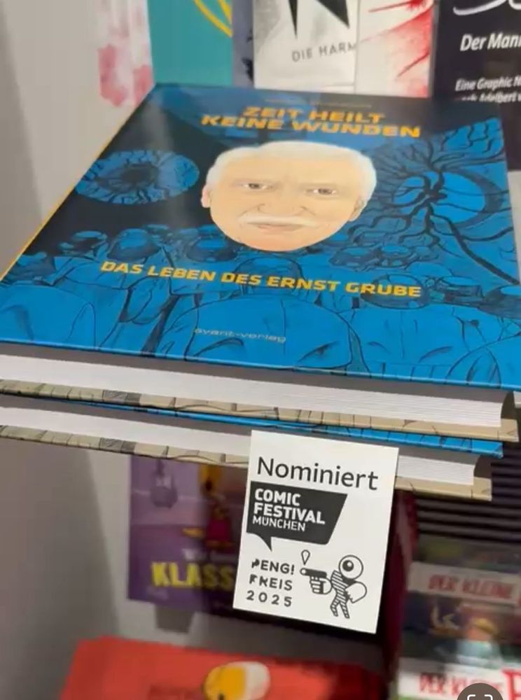 Ein Buch liegt im Regal mit anderen Büchern. An dem Buch klebt ein Zettel mit der Aufschrift „Nominiert. Peng-Preis 2025“. 