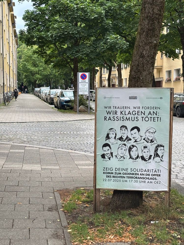 Ein Plakat mit der Ankündigung der Gedenkveranstaltung und Illustrationen der Porträts der neun Opfer steht an einer Straße.