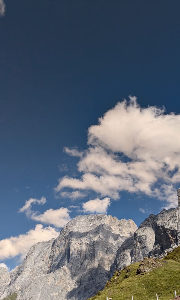 Eine Beegwand beschrienen von der Sonne: Fels und der Himmel verfärbt sich darüber ins Tintenblaue. Wolken bilden sich über den Felsen. 