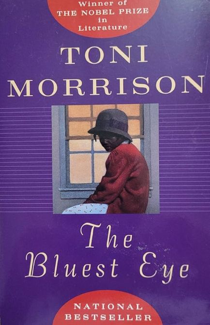 Cover of 'The Bluest Eye' by Toni Morrison. Purple book cover background. In the centre, a square picture of a young black woman in a bowler-hat, red cardigan and white printed skirt. The words read from top of cover to bottom of cover: Winner of the Nobel Prize in Literature, Toni Morrison, The Bluest Eye, National Bestseller.