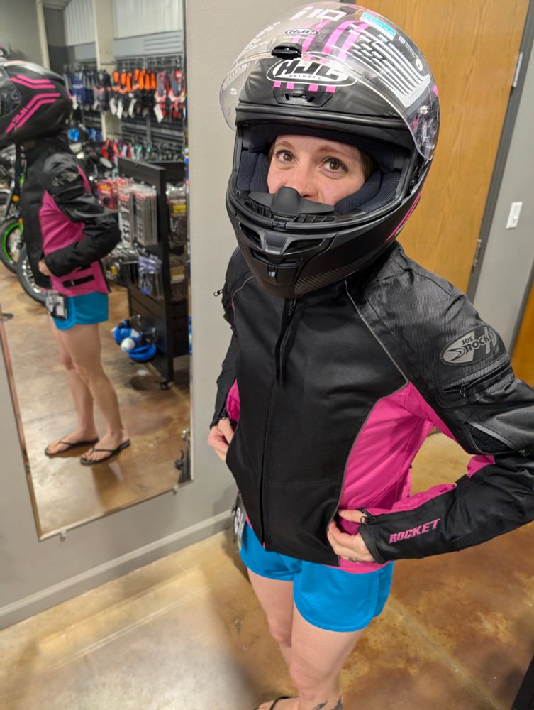 A woman in blue shorts, a black and pink jacket, and a black and pink helmet. 