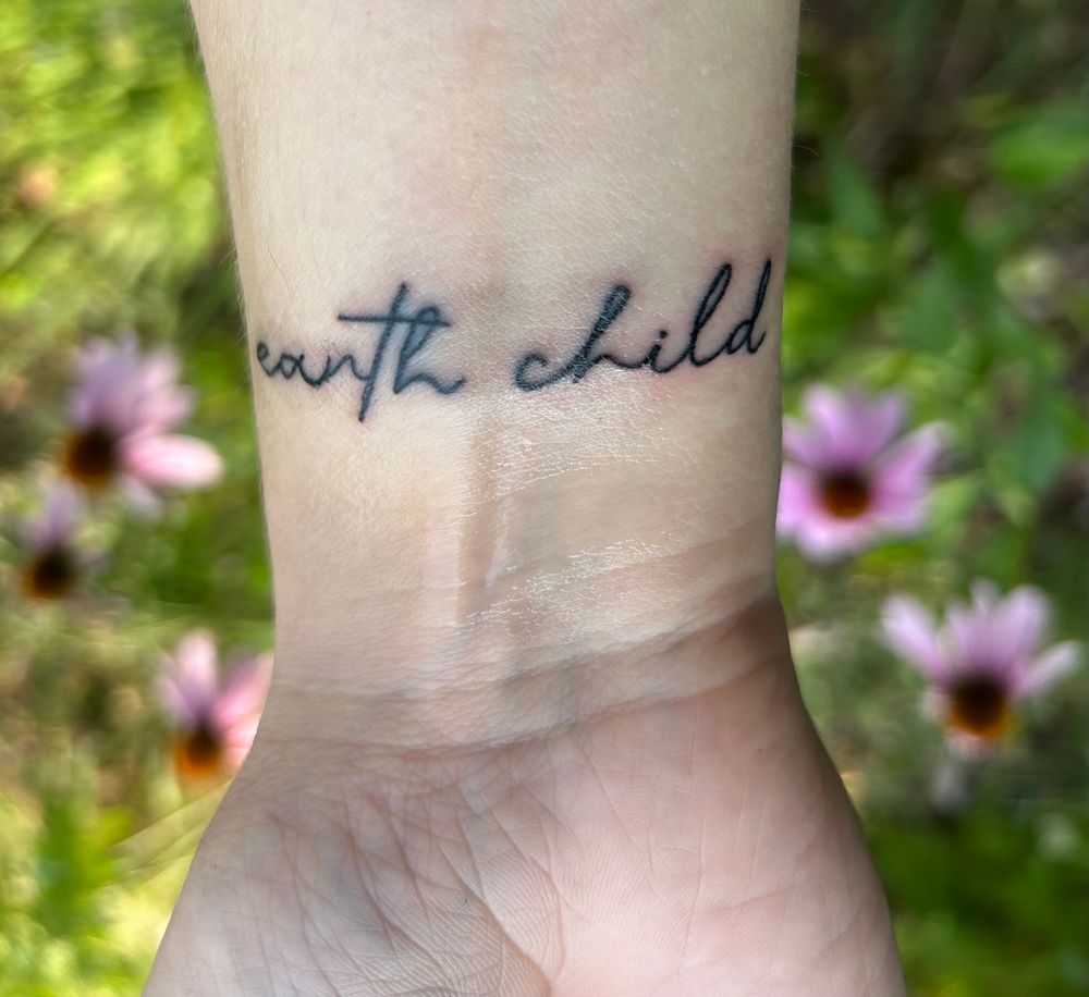 Cursive text tattoo on a white wrist that reads “earth child.” 