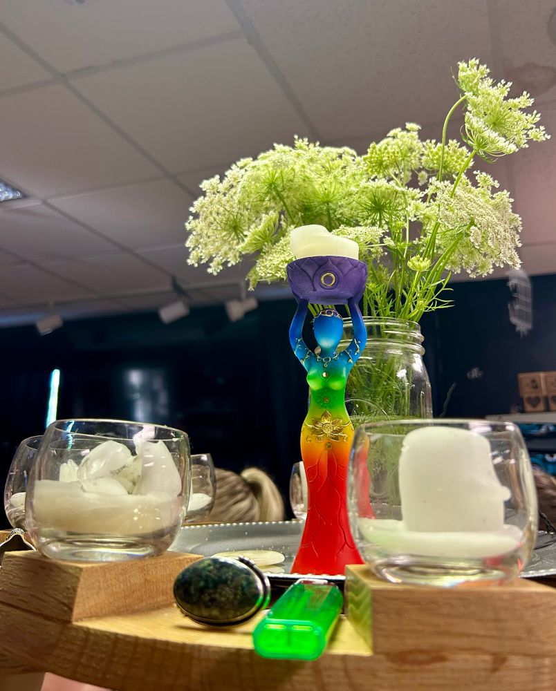 An altar with a rainbow goddess statue, flowers, and candles. 