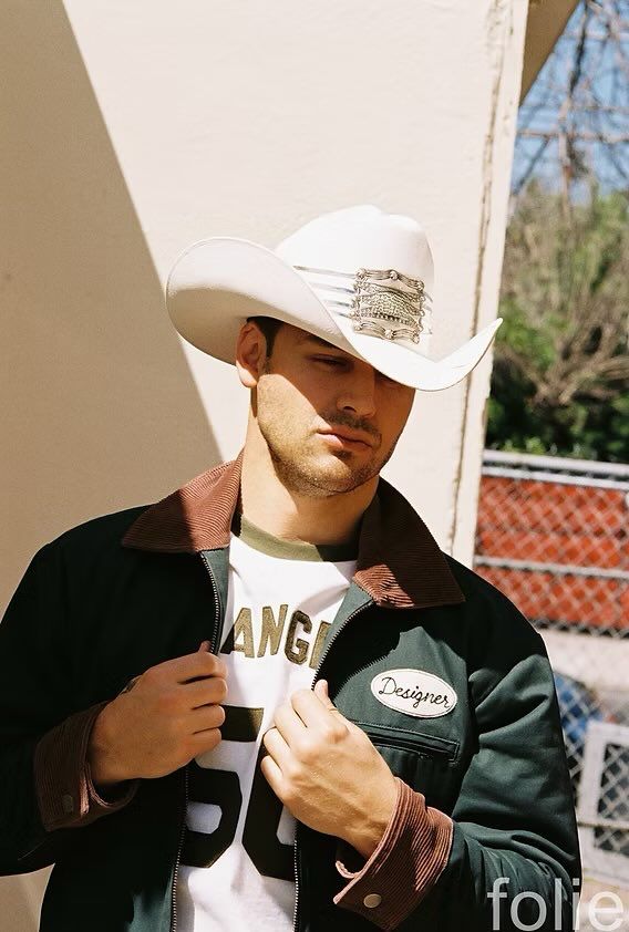 ryan guzman in a cowboy hat, holding on to the side of his jacket 