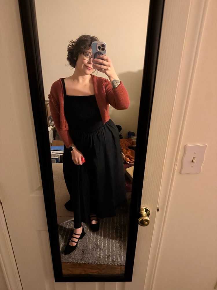Selfie in a mirror with a black dress strappy black heels and a rose matter colored cardigan 