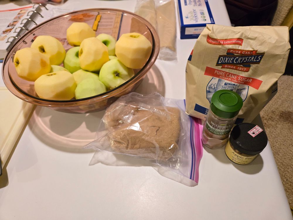 A bowl of peeled apples (Granny Smith and Honeycrisp), brown sugar, granulated white sugar, cinnamon and apple pie spices
