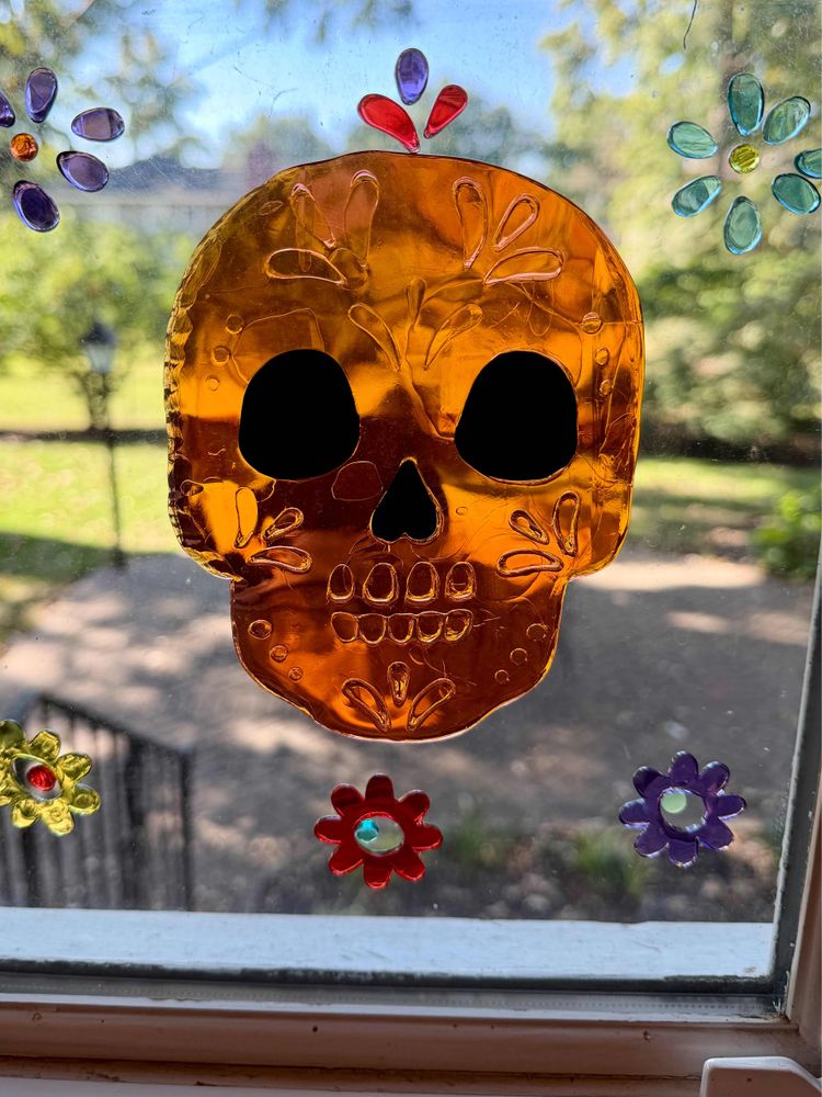 An orange skull decoration with black eyes and a red flower on a window.