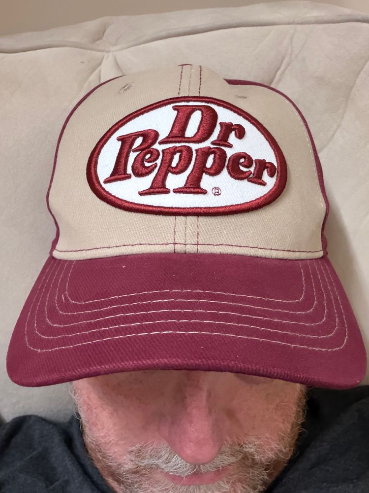 A man wearing a maroon and beige baseball cap with a Dr. Pepper logo.