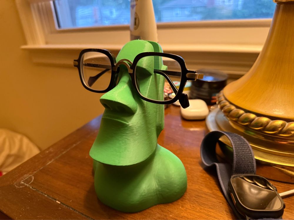 Green 3D printed Moai statue holding glasses on a night stand