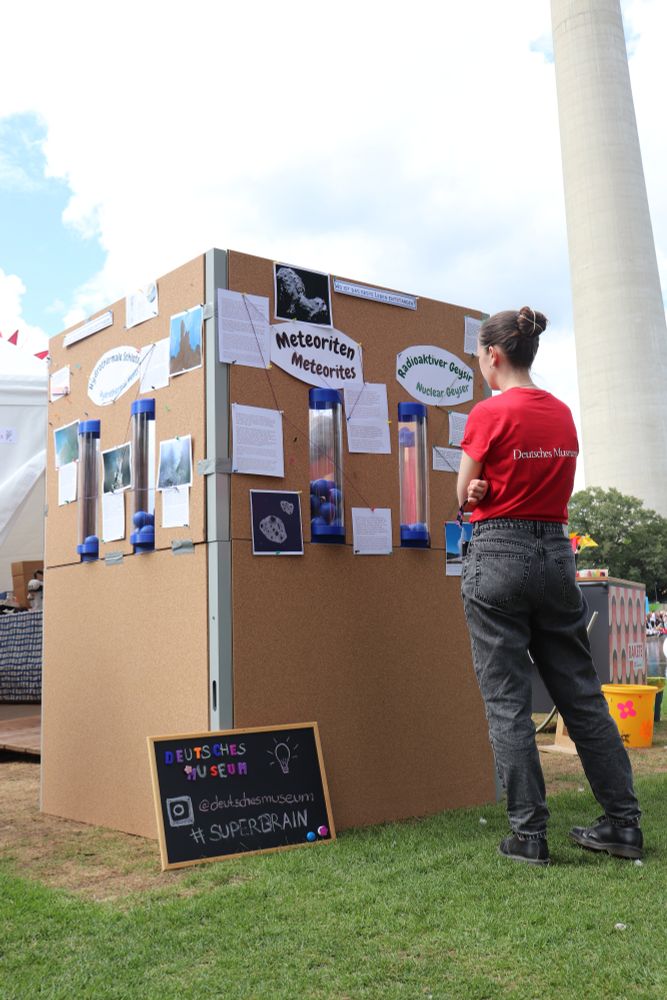 A visitor wearing a red shirt examines the interactive origin-of-life installation, which displays different environments like “Meteorites” and “Nuclear Geyser” for visitors to vote on.