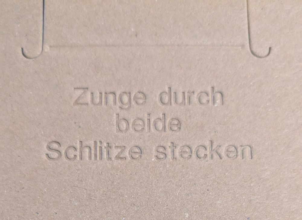 Teil eines Päckchens mit dem eingestanzten Hinweis: Zunge durch beide Schlitze stecken
