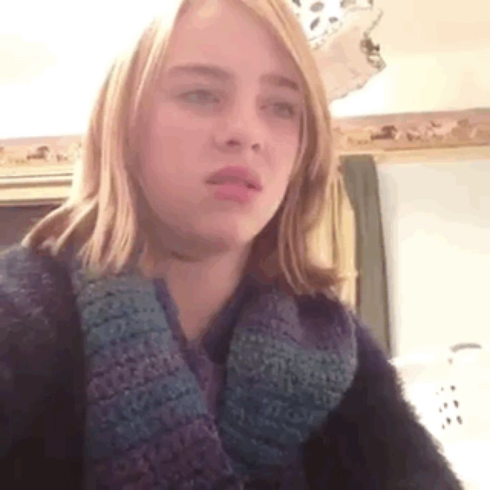 a young girl with long blonde hair is wearing a scarf and a sweater .