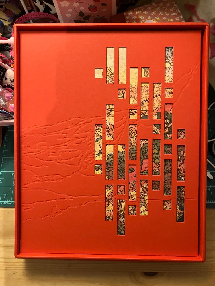 the front slipcover of how a game lives, which is red and textured with small cutouts showing the cover illustration. please excuse the bad lighting in my room i didn’t wanna wait till the sun came back up to post about this lol