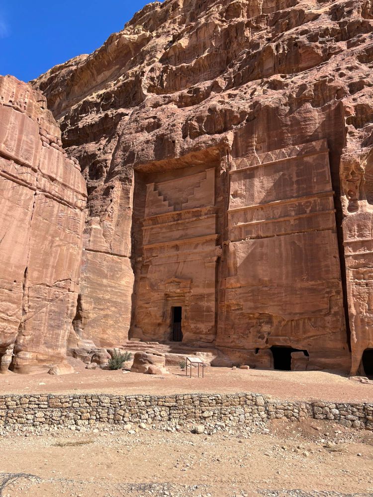 Large tomb structures cut into the pink sandstone cliff. Lower door way above which there are a side view of steps leading upwards - all carved into the rock. 