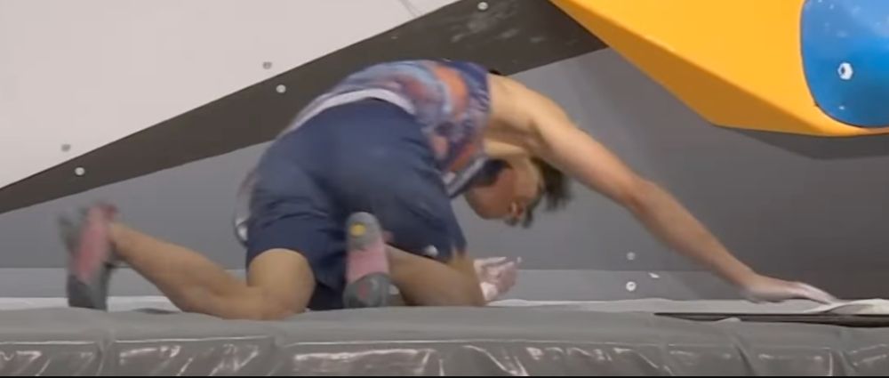 Meichi Narasaki crawls around on the mats to get his chalk bag 