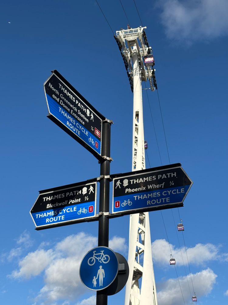 Black and blue signage pointing in three directions with blue skies and a cable car above.