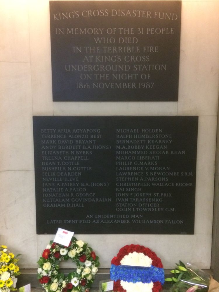 Two plaques to those lost in the Kings Cross fire, the first outlining the event , the second listing those who died.  Below some wreaths and flowers - the photo was taken just after the 30th anniversary.

KINGS CROSS DISASTER FUND IN MEMORY OF THE 31 PEOPLE
WHO DIED IN THE TERRIBLE FIRE AT KINGS CROSS
UNDERGROUND STATION
ON THE NIGHT OF 18th NOVEMBER 1987

BETTY AFLA AGYAPONG
TERRENCE ALONZO BEST
MARK DAVID BRYANT
ANDY BURDETT B.A.(HONS)
ELIZABETH N.BYERS
TREENA CHAPPELL
DEAN T. COTTLE
SUSHEILA N.COTTLE
FELIX DEARDEN
NEVILLE H.EVE
JANE A.FAIREY B.A. (HONS)
NATALIE A.FALCO
JONATHAN R.GEORGE
KUTTALAM GOVINDARAJAN
GRAHAM D.HALL
MICHAEL HOLDEN
RALPH HUMBERSTONE
BERNADETT KEARNEY
M.A.BOBBY KEEGAN
MOHAMMED SHOIAB KHAN
MARCO LIBERATI
PHILIP G.MARKS
LAURENCE V. MORAN
LAWRENCE S. NEWCOMBE S.R.N.
STEPHEN A.PARSONS
CHRISTOPHER WALLACE ROOME
RAI SINGH
JOHN F.JOSEPH ST. PRIX
IVAN TARASSENKO
STATION OFFICER
COLIN J. TOWNSLEY G.M.
AN UNIDENTIFIED MAN
LATER IDENTIFIED AS ALEXANDER WILLIAMSON FALLON

