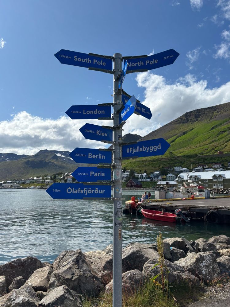 A signpost indicating directions and distances to places around the world.  The one to the North Pole is bent.
