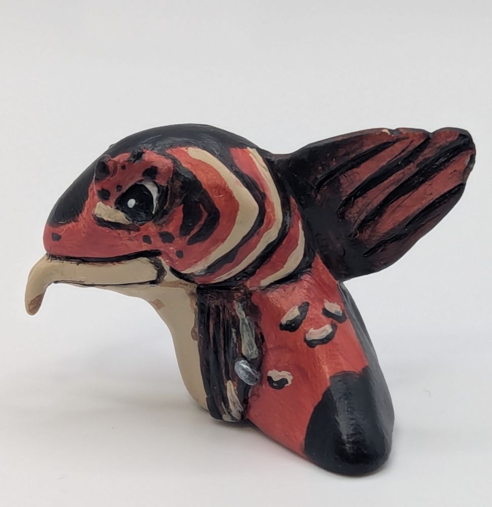 A polymer clay statute of a anthropomorphic fish person. His colours are primary a blue black, brighter red brown, and tan. He has a cute little pipe.