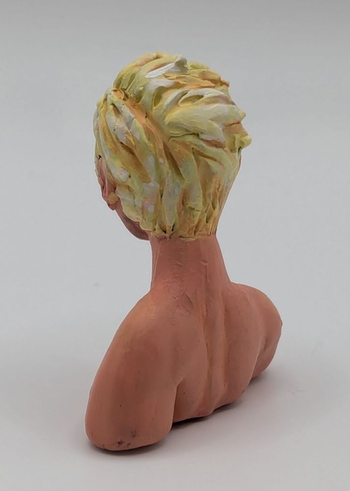 A polymer clay bust of a Caucasian blonde man. He has blue eyes and slightly unkept but combed hair. He is leaning slightly forward. He has stubble and chest hair.