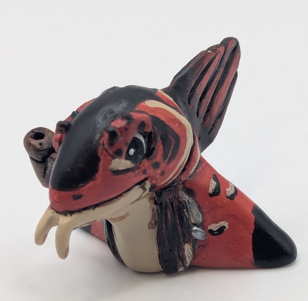 A polymer clay statute of a anthropomorphic fish person. His colours are primary a blue black, brighter red brown, and tan. He has a cute little pipe.