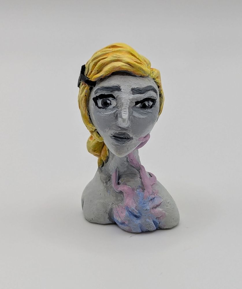 A clay bust of a human female. She has a limited greyscale pallet save for her blonde hair and a strange pink and blue biological growth on her chest.