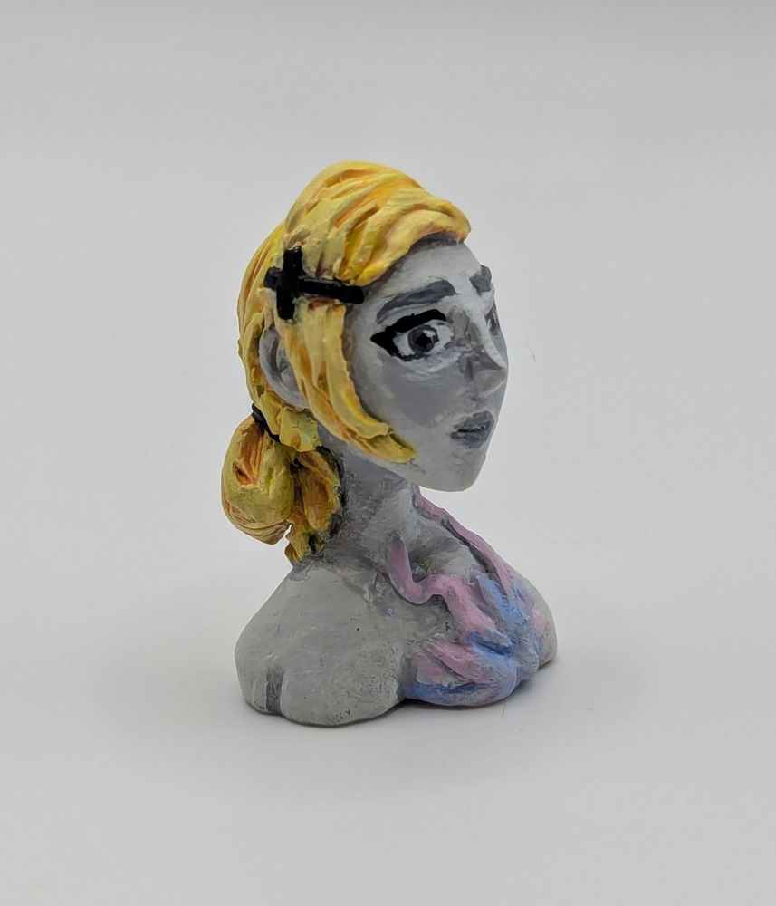 A clay bust of a human female. She has a limited greyscale pallet save for her blonde hair and a strange pink and blue biological growth on her chest.