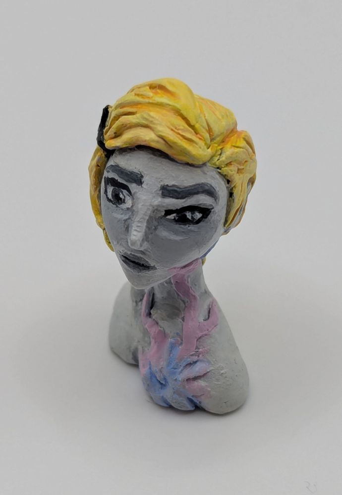 A clay bust of a human female. She has a limited greyscale pallet save for her blonde hair and a strange pink and blue biological growth on her chest.