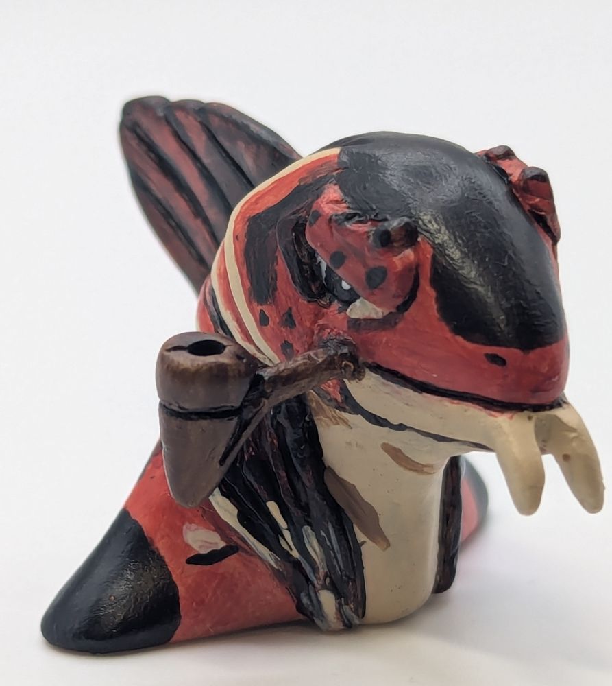A polymer clay statute of a anthropomorphic fish person. His colours are primary a blue black, brighter red brown, and tan. He has a cute little pipe.