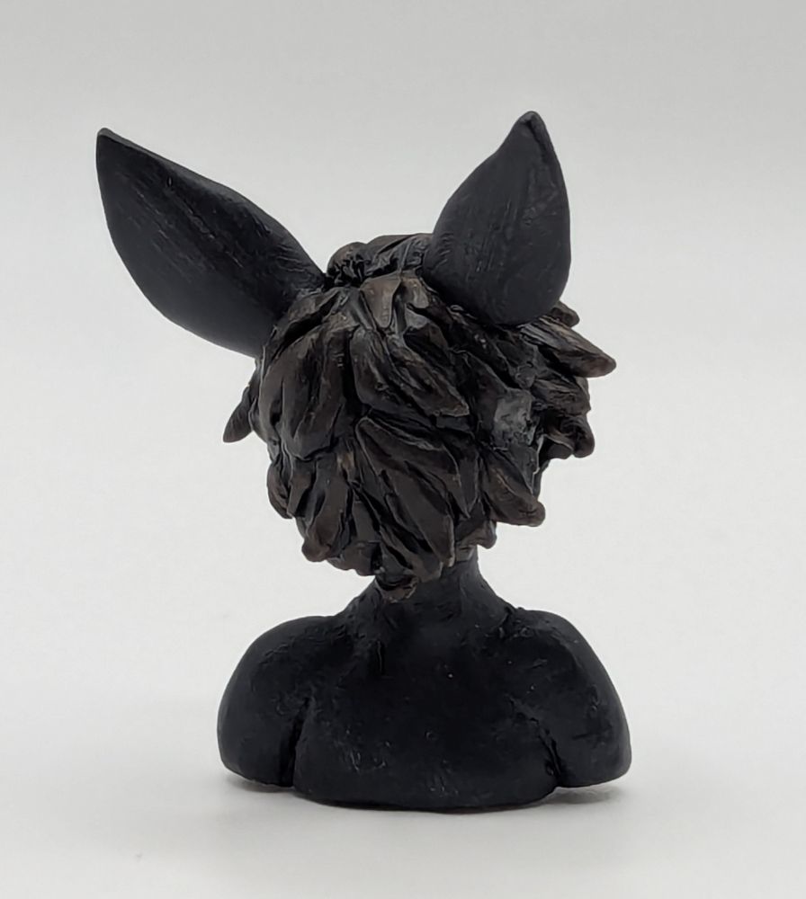 A polymer clay of an anthopormophic bat. She has her tongue sticking out in a playful expression, her bangs cover one eyes. She is a majority black and white, with pink inner ears, nose and eyes.