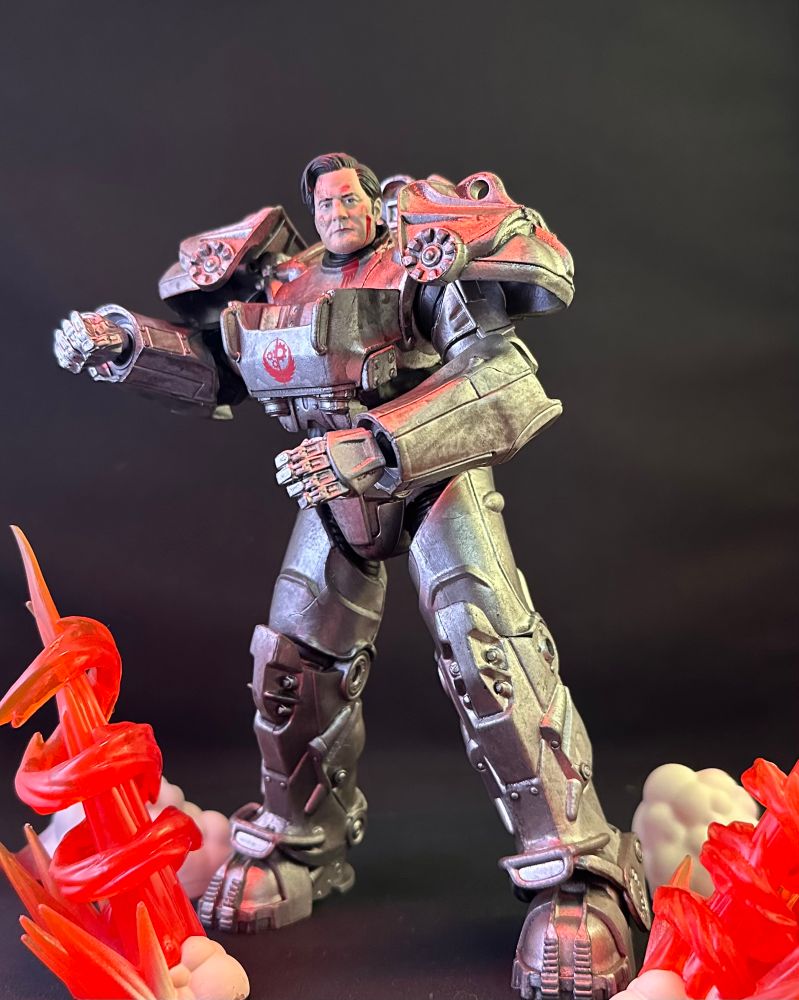 an action figure of Kyle MacLachlan as Hank MacLean from the Fallout TV show, suited in power armor, with toy explosions going off around him