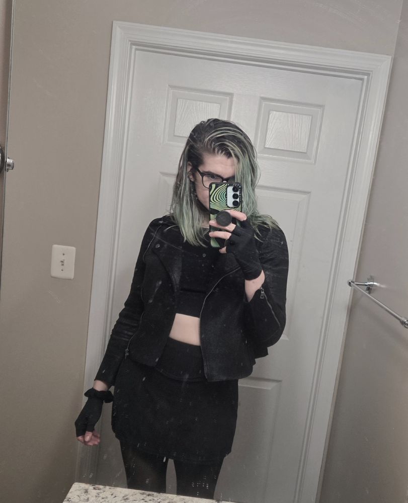 mirror selfie of a goth girl wearing tights, a miniskirt, a crop top and a leather jacket. she has shoulder length green hair 