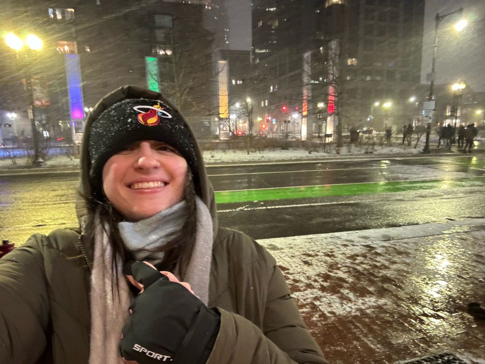 Nicole is all bundled up wearing a black Miami Heat beanie and smiling as it snows.