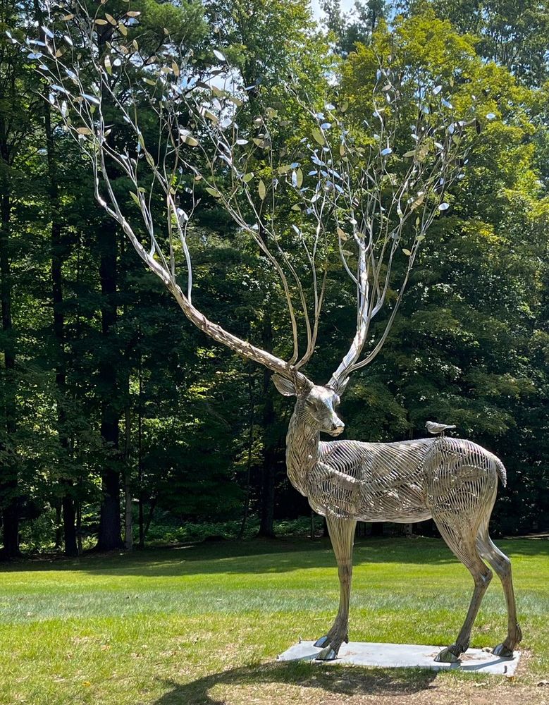 Metal sculpture of a deer with enormous antlers that turn into branches.