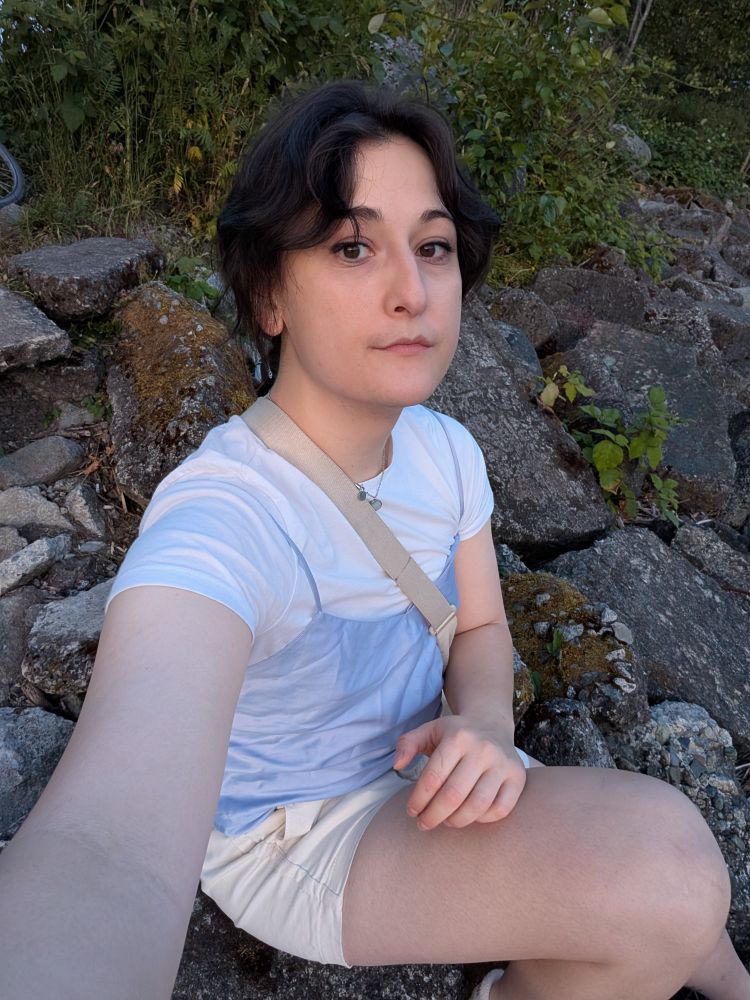 steph taking a selfie on some rocks wearing a white shirt and lilac cami