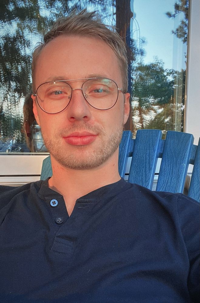 Noah’s cute face with wire rim 70s inspired glasses, blue eyes, and DSLs. On a deck while the sun is setting.  