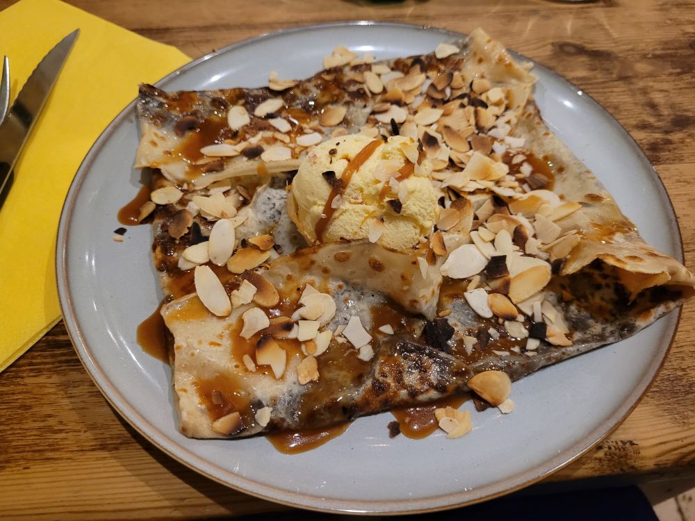 Photo of a crepe with chocolate, caramel, almonds, and ice cream. 