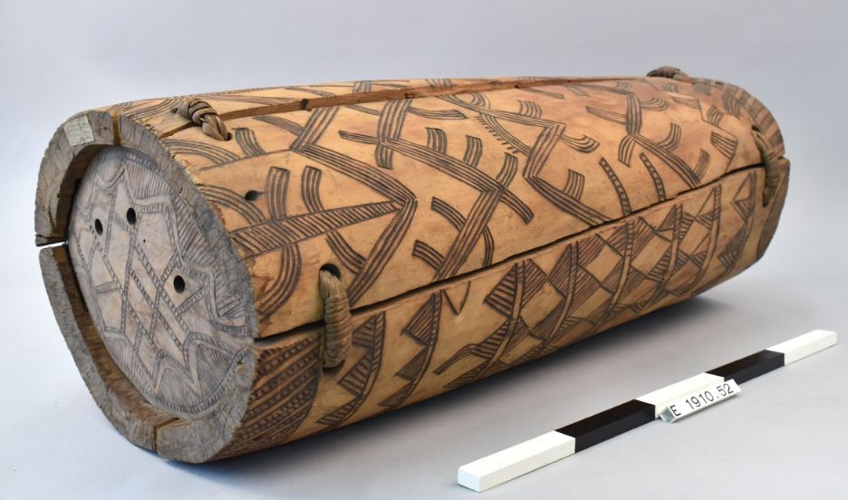 A cylindrical wooden beehive with each end closed by a wooden disc. It is decorated with a pattern which has been burnt into the surface of the wood. Cracks have been repaired with plant fibre loops.